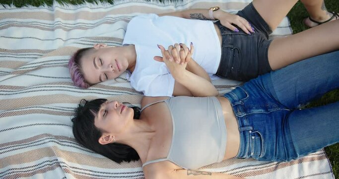 Happy loving lesbian LGBT couple lie on the bedspread in the park and holding hands