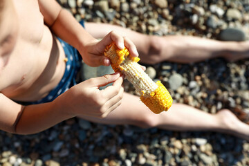 Child has boiled corn on beach