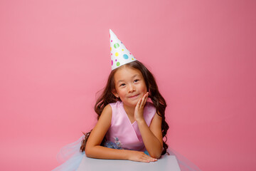 a little girl of Asian appearance with a cap on her head celebrates her birthday on a pink background