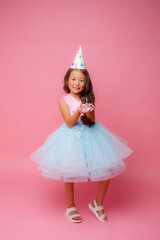 A young Asian girl at a birthday party holds a cake with a candle on a pink background