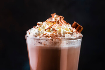 Winter hot chocolate cocoa drink in tall glass with ispices and whipped cream on black table. Dark...
