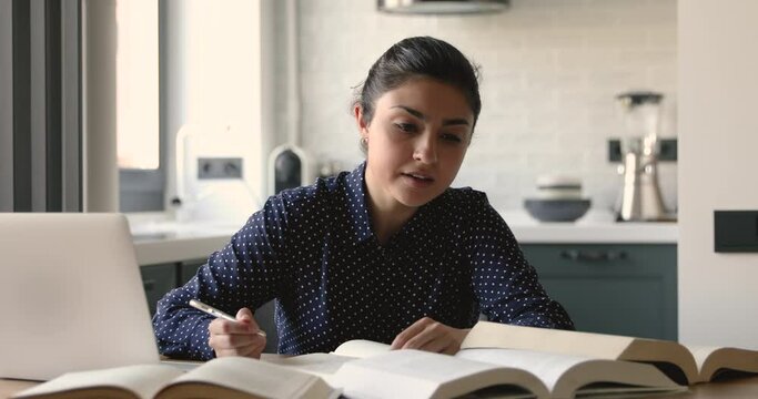 Focused attractive indian ethnicity student girl sit at desk at home noting writing down information take it from textbooks, preparing for college test or university admission, studying hard concept