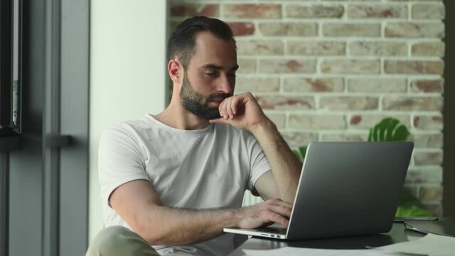 Young serious sad man using laptop computer indoors at home