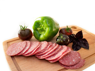 sausage slicing and fresh vegetables in the form of dark tomatoes, green paprika and fragrant purple basil on a wooden cutting doske. selective focus. isolate on white.