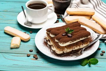 portion of Classic tiramisu dessert, cup of coffee and savoiardi cookies on wooden background