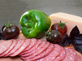 ringed sausage, ripe cherrmy tomatoes, basil leaves and green paprika on a gray background. selective focus.