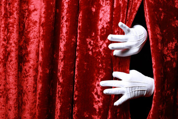 Human hand in white glove opening red velvet curtain