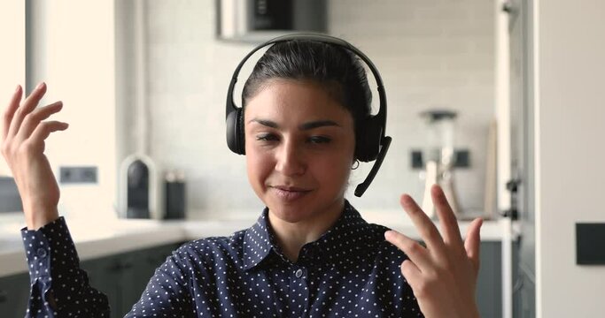Head shot portrait indian 30s woman sit at home wear headset talks looking at camera pass job interview using videocall distant communication. Conversation by video conference app, modern tech concept
