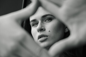 Beautiful woman making a hand frame over gray background. Black and white