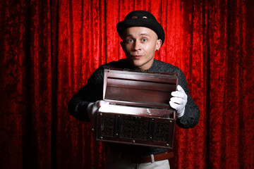 Funny young man in bowler hat and white gloves open treasure chest with gold shining on his face at...