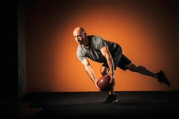 Middle aged Caucasian man performing exercise with medicine ball inside a gym.