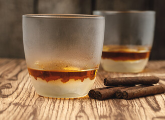 Glass of whiskey and rolled cigars on wooden table