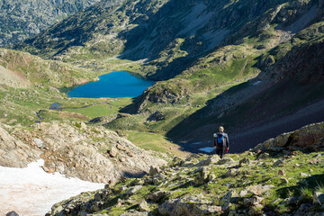Fototapeta na wymiar randonneur en montagne avec vue plongeante sur un lac bleu et des prairies