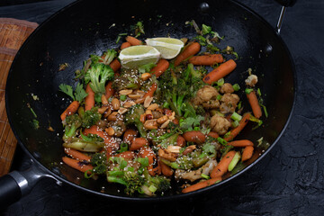 Vegan carrot, broccoli and cauliflower stir fry with nuts and seeds, black wok