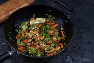 Vegan carrot, broccoli and cauliflower stir fry with nuts and seeds, black wok, copy space
