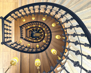 Round spiral staircase with gray walls black railings and yellow lanterns down view