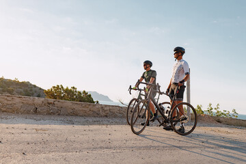 Two male cyclists stand on the road and have a rest