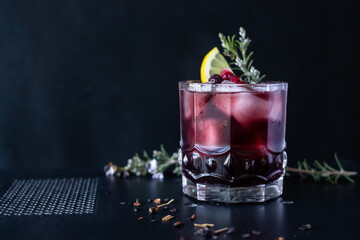 Dark cocktail made with red wine and berries with rosemary and lemon garnish. Dark background.