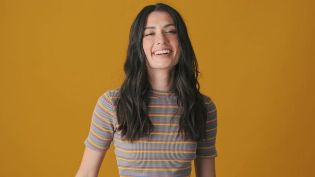 A smiling young woman is showing secret gesture standing isolated over yellow background