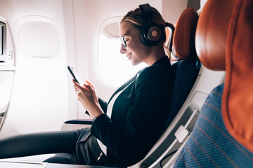Delighted businesswoman messaging on smartphone in airplane
