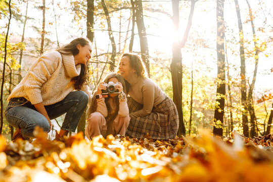 A beautiful couple of lesbian ladies having fun in the autumn forest with retro camera. The young homosexual family with their adopted teenage daughter posing for photo.