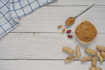 Top view of peanut butter in white ceramic cup placed on white wooden background.