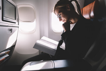 Delighted relaxed woman reading book with interest in plane