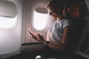 Cheerful adult woman using smartphone in airplane