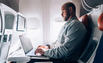 Serious adult businessman using laptop in airplane