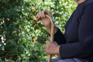 Elderly woman holding wooden walking stick in the park