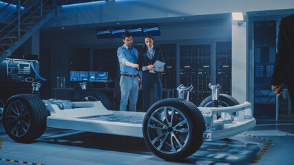 Fototapeta na wymiar Auto Industry Design Facility: Male Chief Engineer Shows Car Prototype to Female Car Designer. Electric Vehicle Platform Chassis Concept with Wheels, Engine and Battery.