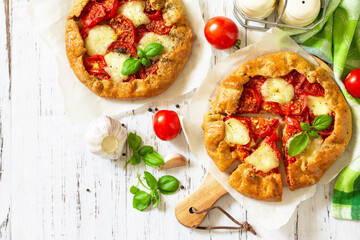 Healthy pastries made from rye flour, diet food. Galette tomatoes, mozzarella and basil on a wooden table. Top view flat lay background. Copy space.