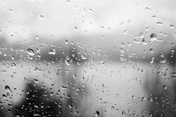 Raindrops on a window, illustrating gray and rainy weather during the day. Black and white grayscale