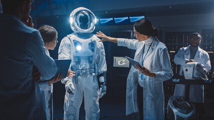 Diverse Team of Aerospace Scientists and Engineers Wearing White Coats have Discussion, Use Computers Design New Space Suit Adapted for Galaxy Exploration and Travel. Constructing Astronaut Suit - obrazy, fototapety, plakaty
