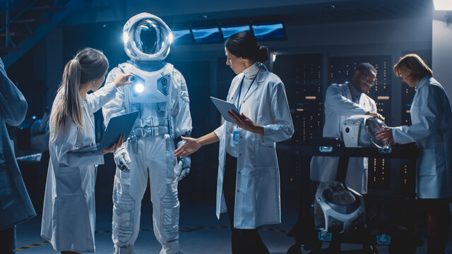 Diverse Team of Aerospace Scientists and Engineers Wearing White Coats have Discussion, Use Computers Design New Space Suit Adapted for Galaxy Exploration and Travel. Constructing Astronaut Suit