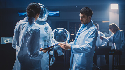 Diverse Team of Aerospace Scientists and Engineers Wearing White Coats have Discussion, Use Computers, Construct Astronaut Helmet for New Space Suit Adapted for Galaxy Exploration and Travel. - obrazy, fototapety, plakaty