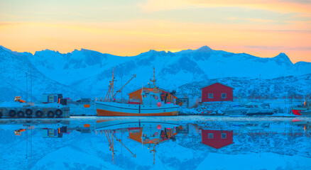 Fisher shelter in winter with fishboat at sunset in the background snowy mountains and Norwegian fjords - Tromso, Norway