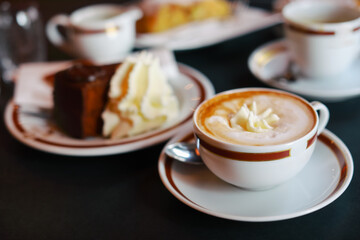 Coffee with cream in cap and with chocolate cake on table in cafe