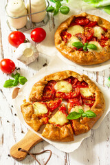 Healthy pastries made from rye flour, diet food. Galette tomatoes, mozzarella and basil on a wooden table.