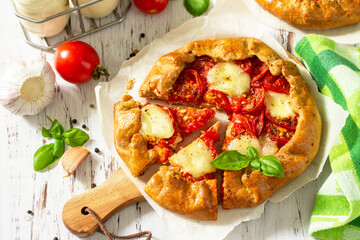 Healthy pastries made from rye flour, diet food. Galette tomatoes, mozzarella and basil on a wooden table.
