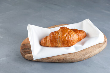 Fresh golden croissant on wooden cutting board. Gray background, copy space