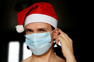 Portrait of man in medical face mask and Santa Claus hat. Christmas celebration during coronavirus pandemic