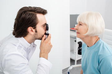 Optometrist doing eye exam to a patient using an ophthalmoscope, cataract diagnostic. Vision...