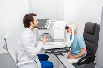 Concentrated optometrist checking eye for a patient using modern equipment. Eye exam and vision...