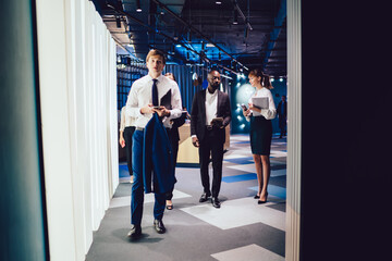 Group of diverse male and female colleagues walking to cooperate conference meeting for discussing business planning, professional traders dressed in formal wear communicating in office hallway