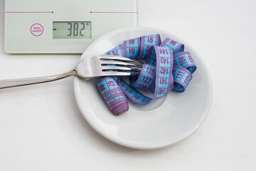 Diet and weight loss concept. Scales, blue measuring tape in a white plate wound on a fork on a...