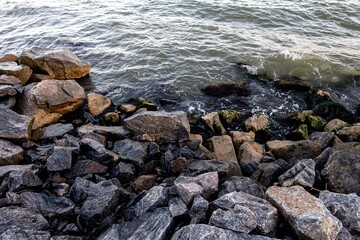 stone and sand seashore with waves in the sunset light