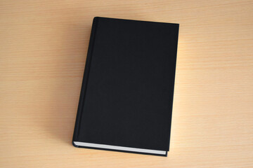 Fototapeta premium Blank black book on a light wood background