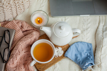 Laptop, face mask, hot tea mug, candle, glasses, kettle, wooden stand. Quarantine. Home Office. Cozy breakfast. Fall.