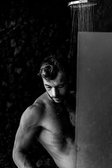 Topless handsome man taking a shower washing hair with shampoo product under water falling from luxury outdoor rain shower head.